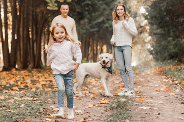 Obraz premium Happy beautiful family with dog labrador is having fun together walking the in park.