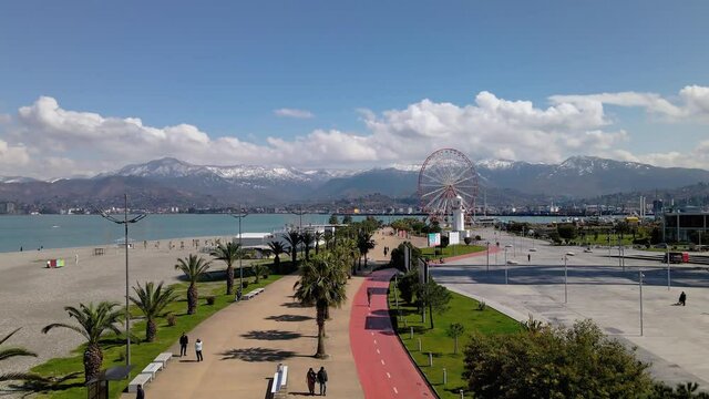 Aerial footage. The drone flies over the modern city embankment of the city of Batumi. Ferris wheel and mountains on the background