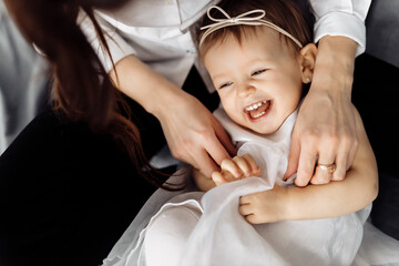 Caucasian loving mother hugging softly and tickling her little girl in charming dress, happiness...