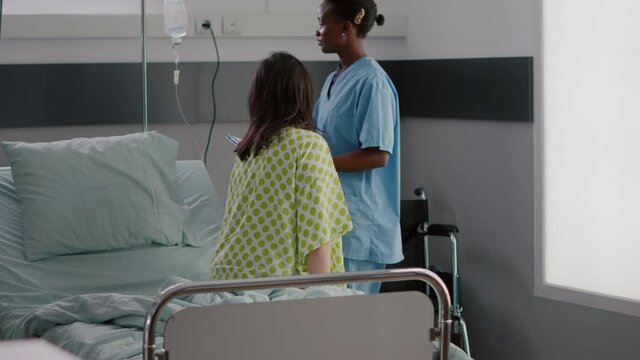 Afro american asisstant monitoring hospitalized sick woman with respiratory illness recovering after medical surgery. African nurse working in hospital ward explaining treatment to patient