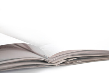 Open folded newspaper lies on a white table. Photographed from a low point of view, very shallow depth of field. Copy space