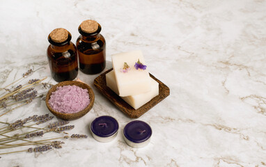 Top view of lavender salt and flower with round purple candle, white soap and bottle of essencail oil on marble table. Coppy space on right.