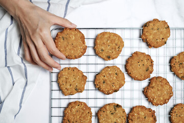 Hand picking cookie from cooling rack on marble background.