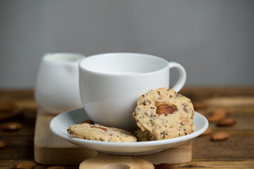 Close up of almond and sesame cookies with white cup of milk on wooden plate.