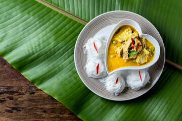 Thai food Green curry in Heart shaped plate and Rice noodles on banana leaves background.