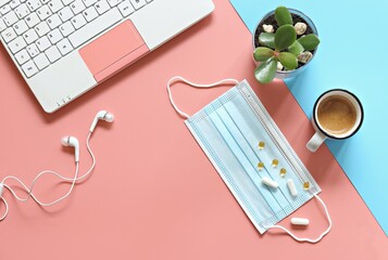 Pastel office desk table with laptop , headphones, protective mask, cup of coffee and small succulent plant on colored background. Work from home. Flat layot, copy space. Selective focus