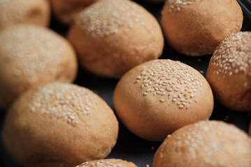many baked sesame topping burger breads lay on oven tray waiting for cooking, shot with shallow focusing  for using as background wallpaper.