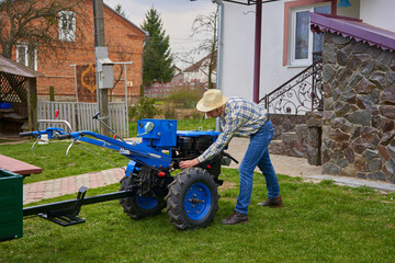 start the tractor with the handle,man with a handle starts a two-wheeled tractor, starting the tractor engine - obrazy, fototapety, plakaty