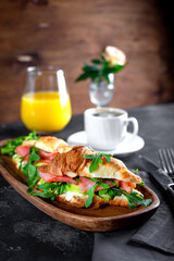  Croissants with arugula, avocado and salmon, a cup of black coffee and a glass of orange juice on the table, breakfast concept with soft focus vertical photo