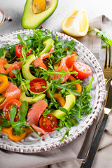 Fresh summer vegetable salad with arugula, tomatoes, bell peppers, avocado and salmon on a plate close up vertical photo