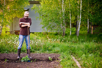Smiling mid adult farmer leaning on garden hoe. Spring work in the garden, transplanting seedlings into the beds. Healthy and eco-friendly family food.