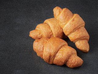 baked french croissants on a brown kitchen board, black background, close-up