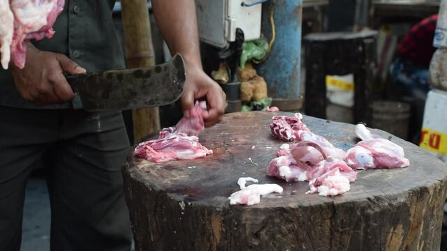 A butcher chopping goat meat with his cleaver at his meat shop