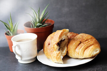 A cup of coffee, a croissant and a cactus in a pot on a black background