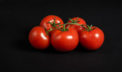 Juicy tomatoes on a black background. Fresh vegetables on a branch. Kitchen. background for restaurant.