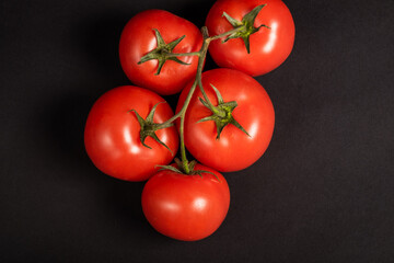Juicy tomatoes on a black background. Fresh vegetables on a branch. Kitchen. background for restaurant.