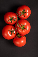 Juicy tomatoes on a black background. Fresh vegetables on a branch. Kitchen. background for restaurant.