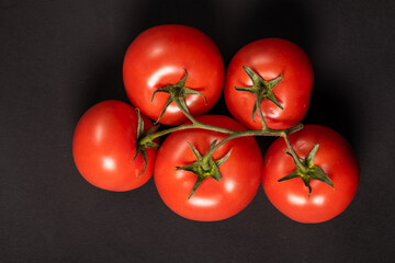Juicy tomatoes on a black background. Fresh vegetables on a branch. Kitchen. background for restaurant.
