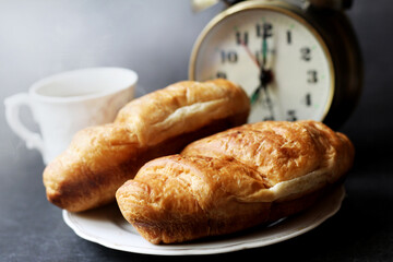 Cappuccino and croissants, alarm clock on black background