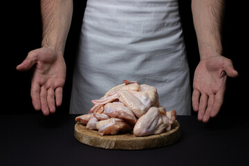 Raw chicken wings on a black background. The chef prepares chicken wings on a dark background. Fresh chicken meat.