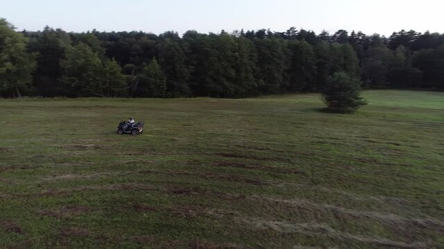 Aerial shot of riding an ATV in a meadow near the forest