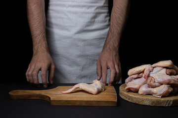 Raw chicken wings on a black background. The chef prepares chicken wings on a dark background. Fresh chicken meat.