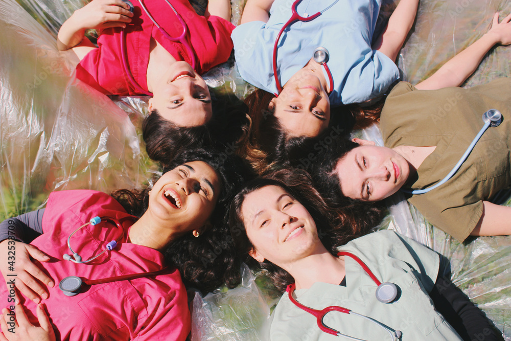 Wall mural Group portrait of doctor / medical student / healthcare worker women smiling and happy outdoors in scrubs with stethoscopes 