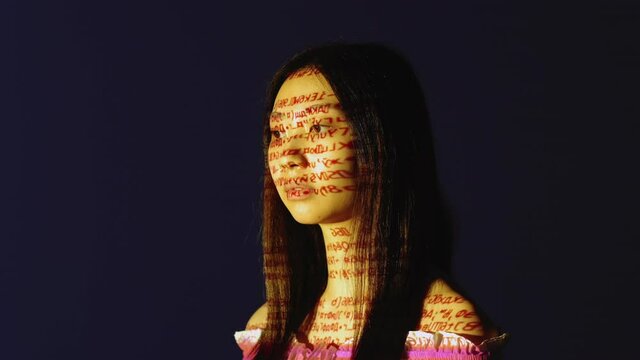 Mind control. Brainwash propaganda. Information analysis. Hypnotized digital glitched Asian woman face in colorful encryption defect noise projector light isolated on dark blue.