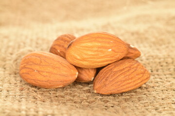 Several grains of peeled raw, organic almonds, close-up, on sacking.