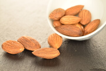 Several grains of peeled raw, organic almonds with white dishes, close-up, on a slate board.