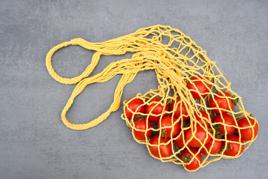 A string bag with red fresh ripe tomatoes. Yellow mesh bag. No waste, no plastic. Eco-friendly concept. Handmade macrame bag. Eco-friendly, zero-waste shopping and healthy lifestyle concept. 