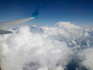 Fluffy clouds over the sky. Scenic view from the airplane window. Natural beauty of blue sky with clouds. Wing of the plane. Airplane flying in the sky.