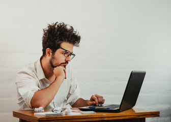 Young Caucasian male staring at the laptop, bored and disheveled during work, resting head on hand