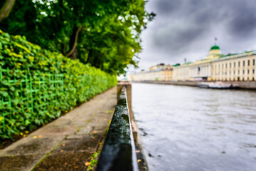 Rainy autumn day in the city, alley in the park near the river. Close up view from the handrail on the embankment level