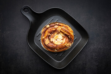 cinnamon almond danish roll in black pan on dark grey texture background
