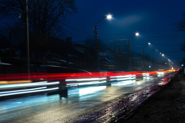 Fototapeta na wymiar night dark photo of blur of intermittent red-blue light from car headlights, along the road with lantern light