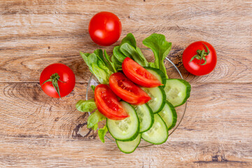 Vegetable slicing of cucumbers and tomatoes on a plate on a wooden background