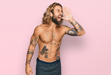 Handsome man with beard and long hair standing shirtless showing tattoos shouting and screaming...