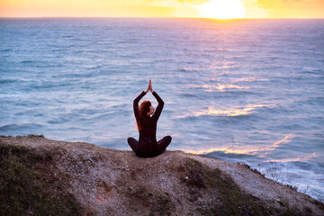 Woman meditating in lotus pose at sunset