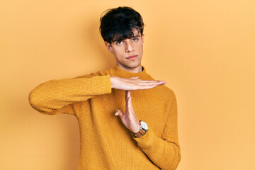 Handsome hipster young man wearing casual yellow sweater doing time out gesture with hands,...