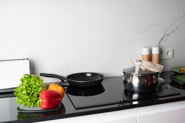 pot and frying pan stands on stove, green salad and pepper lying near it. Preparing meal