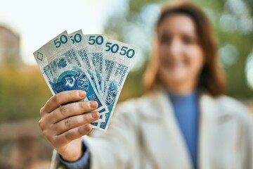 Young hispanic woman smiling happy holding polish zloty banknotes at the park