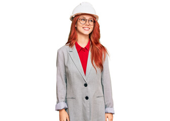 Young redhead woman wearing architect hardhat looking away to side with smile on face, natural expression. laughing confident.