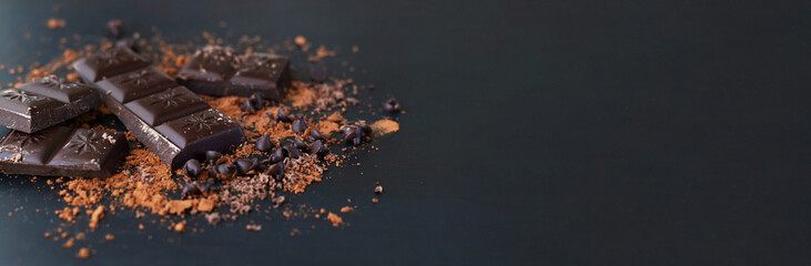 Broken chocolate bar pieces and cocoa powder on dark background