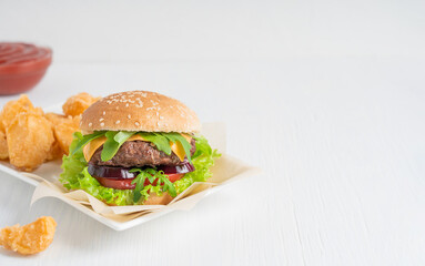 Homemade hamburger sandwich made of beef ground meat, cheese, lettuce, tomatoes and onion inside sliced bun served with fried potato wedges and ketchup on white wooden table. Image with copy space