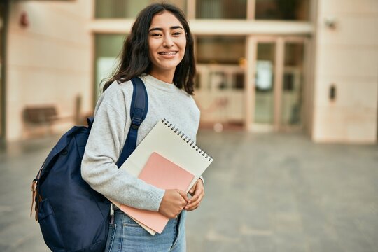 Young middle east student girl smiling happy holding book at the city.