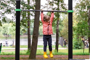 Fototapeta premium a little girl hangs on a horizontal bar in an autumn park