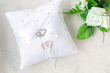 white rose and pillow for wedding rings with rings on white background. cushion for wedding rings with rhinestone hearts