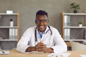 Middle-aged African-American male doctor sits in front of a webcam and conducts an online...