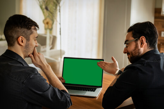 Zwei junge M&auml;nner, Anfang 20. sitzen im Wohnzimmer, schauen auf den Display eines Laptops. Einer zeigt mit den Fingern drauf,  der anderer  ist  nachdenklich. Green screen, gr&uuml;ner Bildschirm
